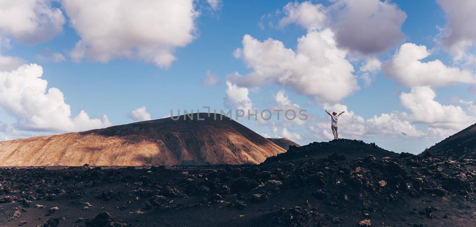 Woman rising hands up in the sky, enjoying amazing views of volcanic landscape in Timanfaya national park on Lanzarote, Spain. Freedom and travel adventure concept