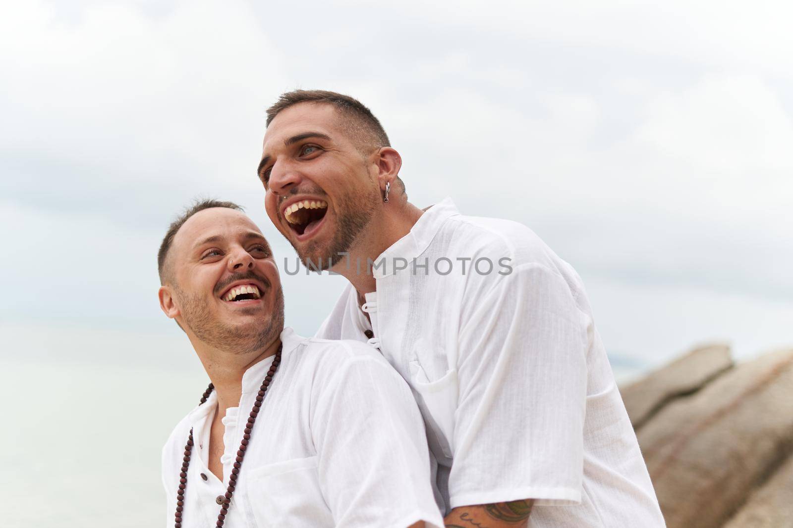 Gay couple laughing distracted while embracing on the beach by WesternExoticStockers