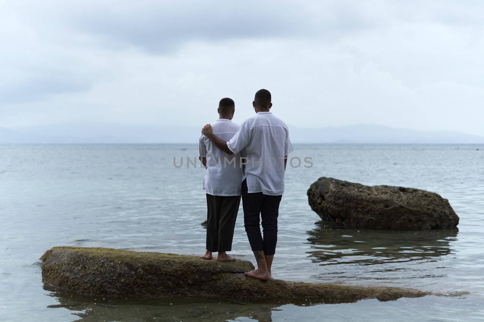 Back of a gay couple standing on a rock looking out to the horizon of the ocean in the evening