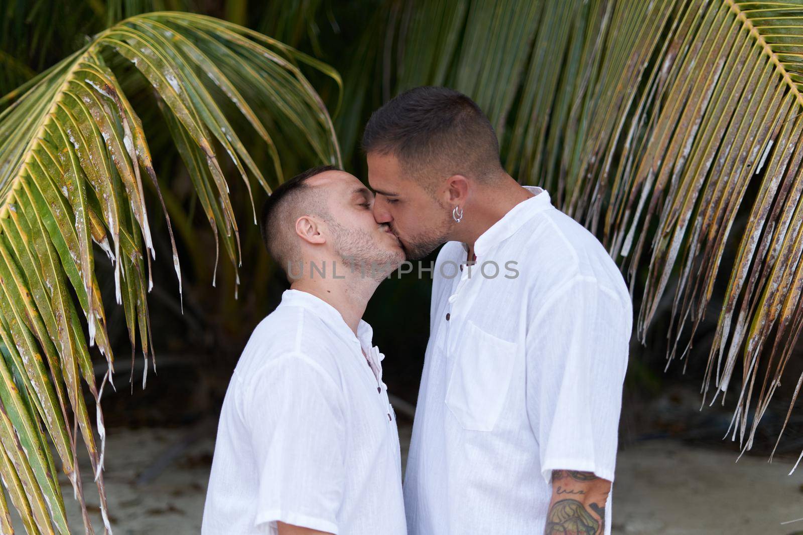 Portrait of a newlywed gay couple in white t-shirt kissing next to a palm tree