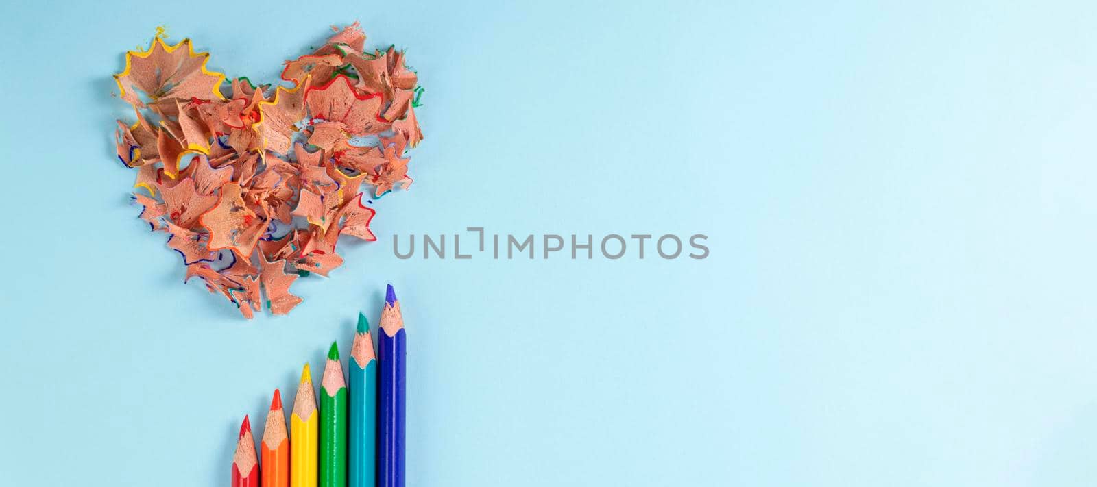 banner with Sharpened colored pencils and heart-shaped pencil shavings on pastel blue color. Rainbow or LGBT pencils. Decoration for St. Valentine's Day. Top view