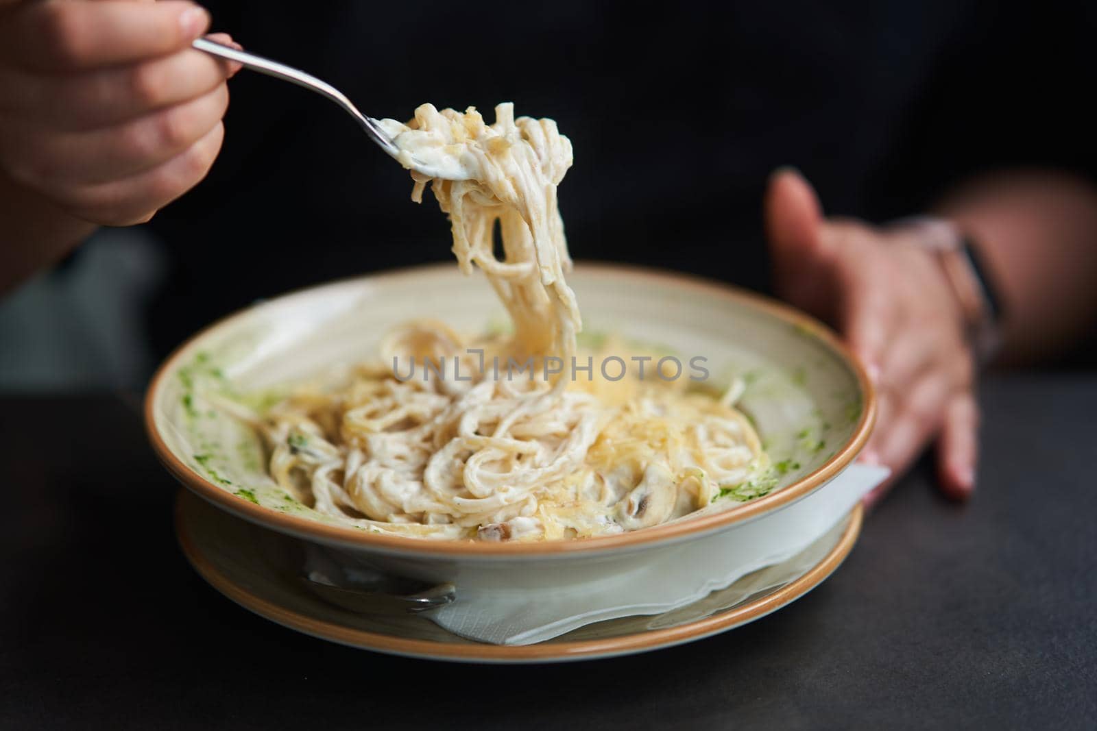 Appetizing carbonara paste with chicken improperly wound on fork. Spaghetti inaccurately hanging and falling from fork. Close up. High quality photo