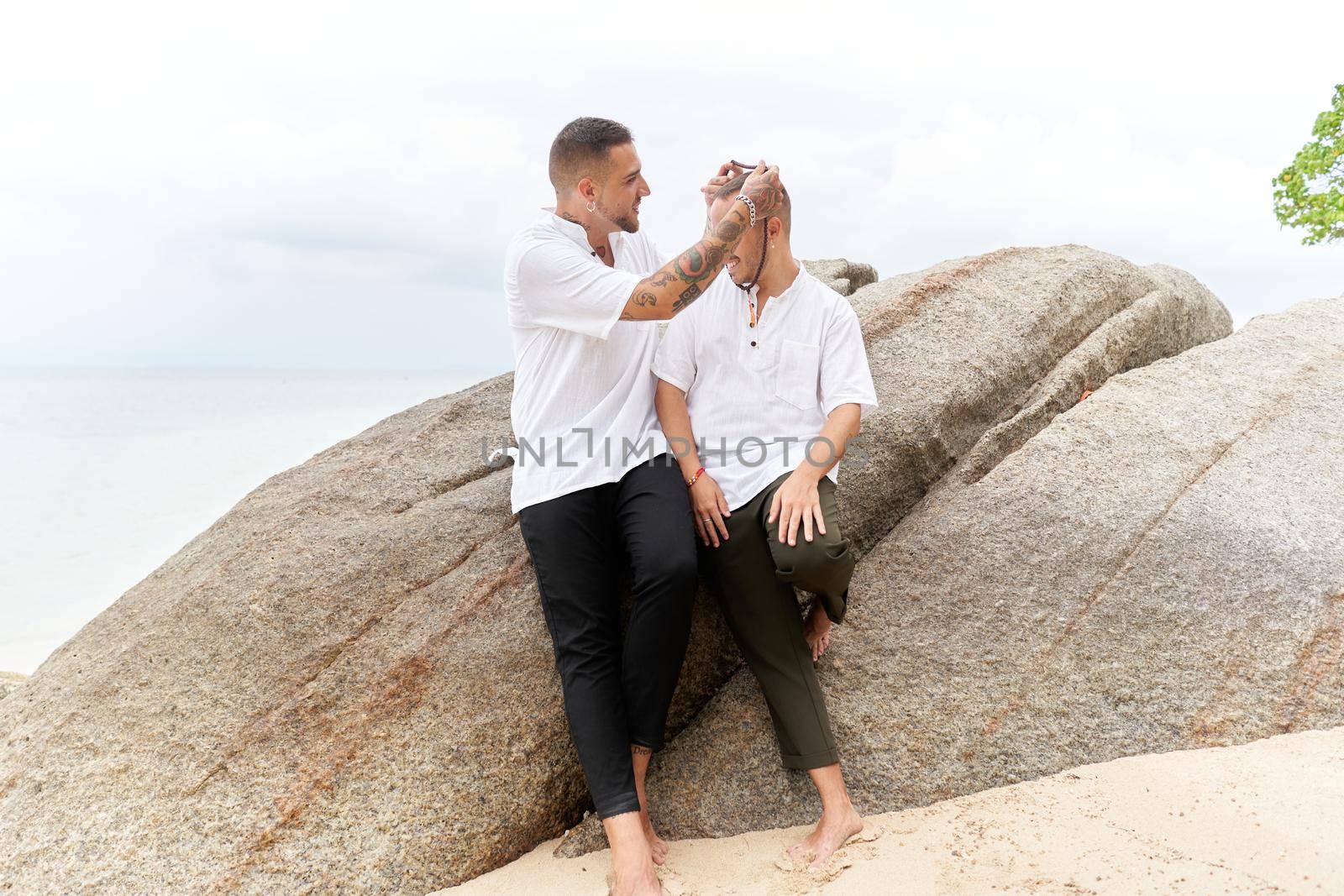 Man putting a necklace around his gay partner's neck on a tropical beach by WesternExoticStockers