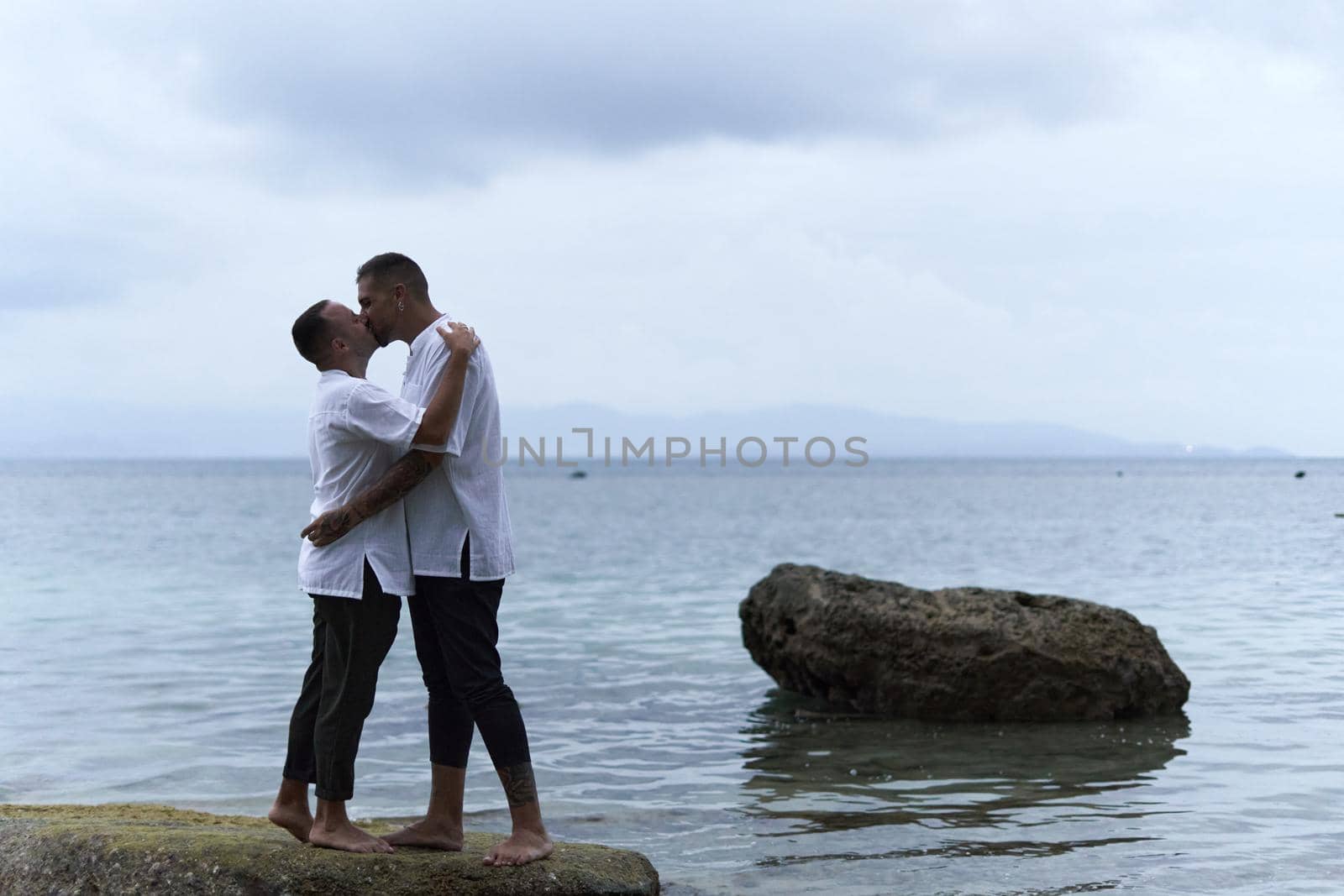 Homosexual couple kissing on a rock facing the sea by WesternExoticStockers
