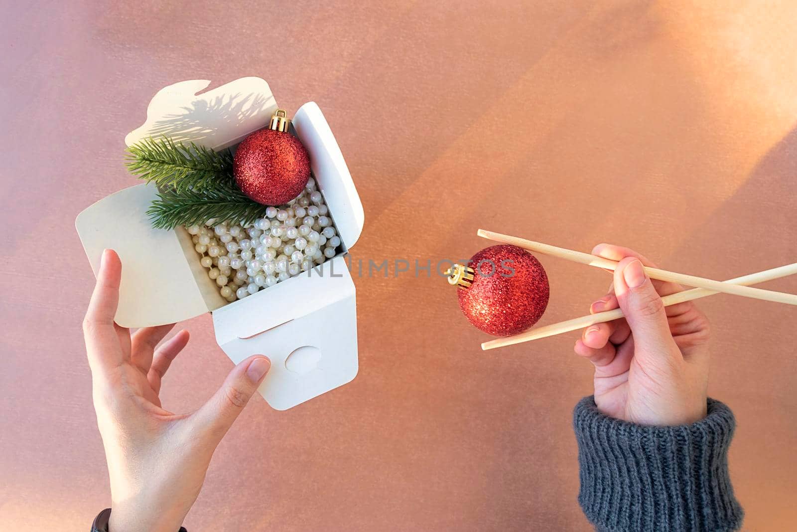 Christmas decorations in box for Chinese noodles. Female hands eat with chopsticks. white beads, branches of Christmas tree and red balls. Asian Chinese or Korean New Year concept. flat lay