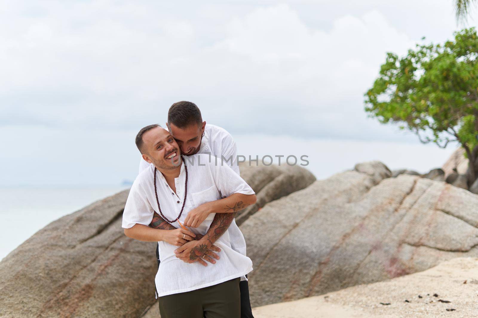 Portrait with copy space of a happy gay couple embracing and laughing on a beach