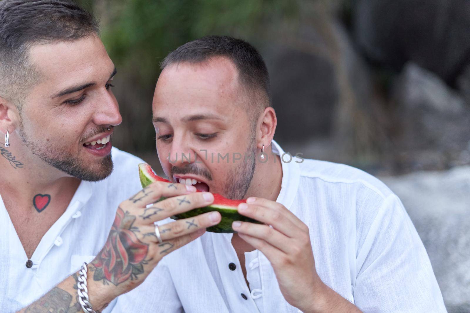 Cropped photo of a man feeding with watermelon to his gay partner in a beach