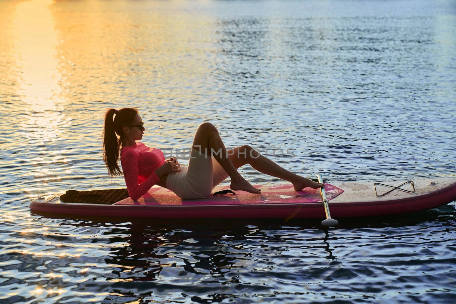 Woman floating on sup board during summer sunset by SerhiiBobyk