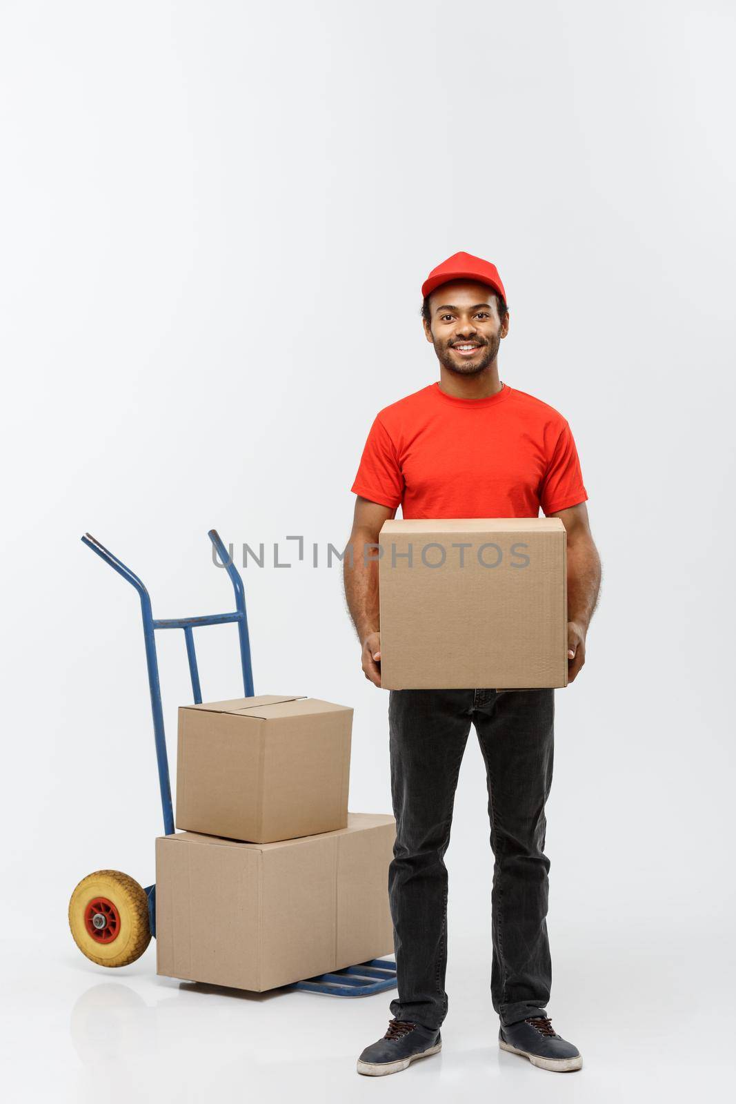 Delivery Concept - Portrait of Handsome African American delivery man or courier with hand truck and holding box. Isolated on Grey studio Background. Copy Space