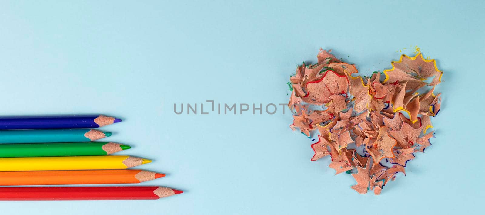 banner with Sharpened colored pencils and heart-shaped pencil shavings on pastel blue color. Rainbow or LGBT pencils. Decoration for St. Valentine's Day. Top view