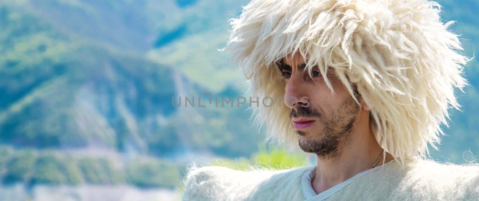 A Georgian man in a hat against the background of mountains and the sky. Selective focus. by yanadjana