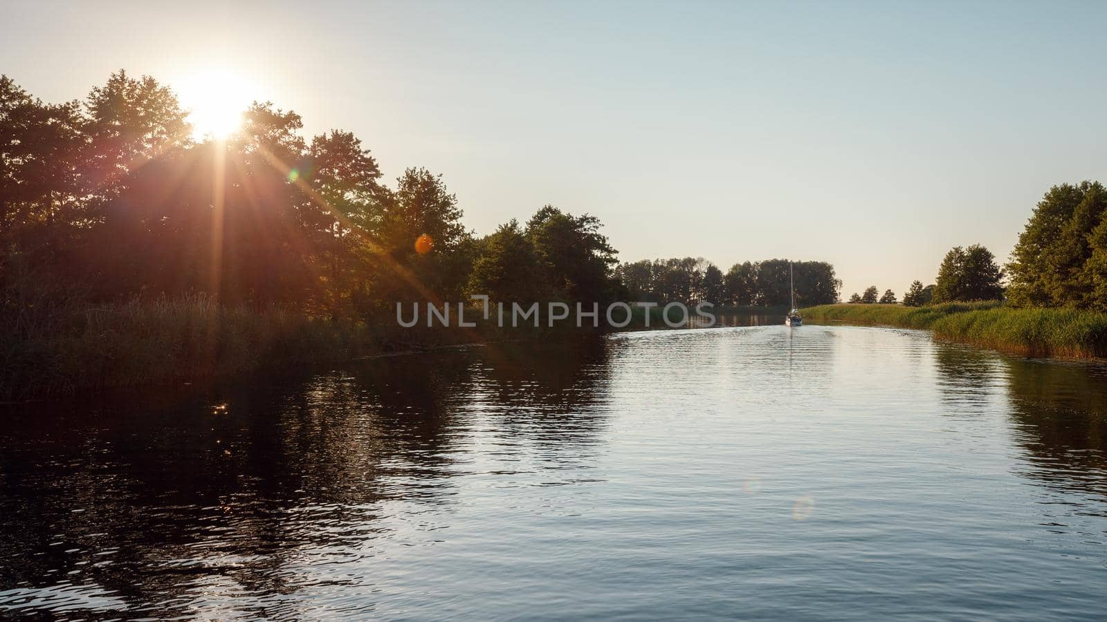 Sunny evening on the river in the countryside. Calm water yacht in the distance