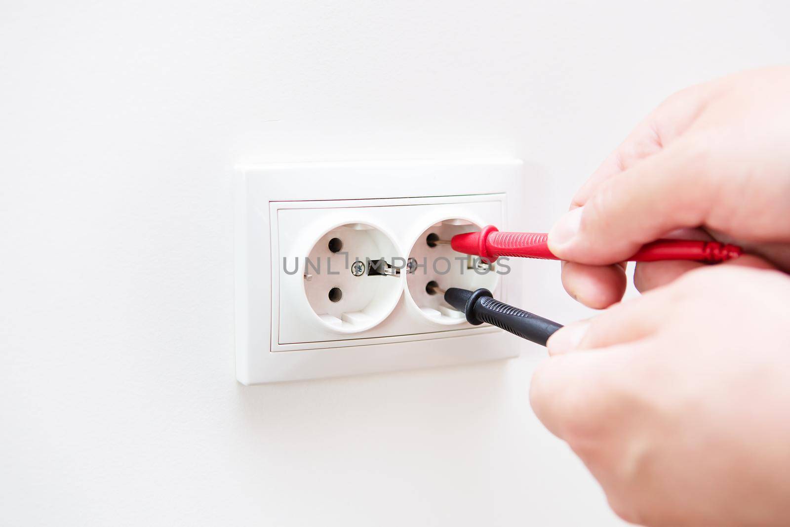 Measuring the voltage in the socket with a professional digital multimeter. Profession electrician, the process of installing sockets. Close-up, selective focus, noise