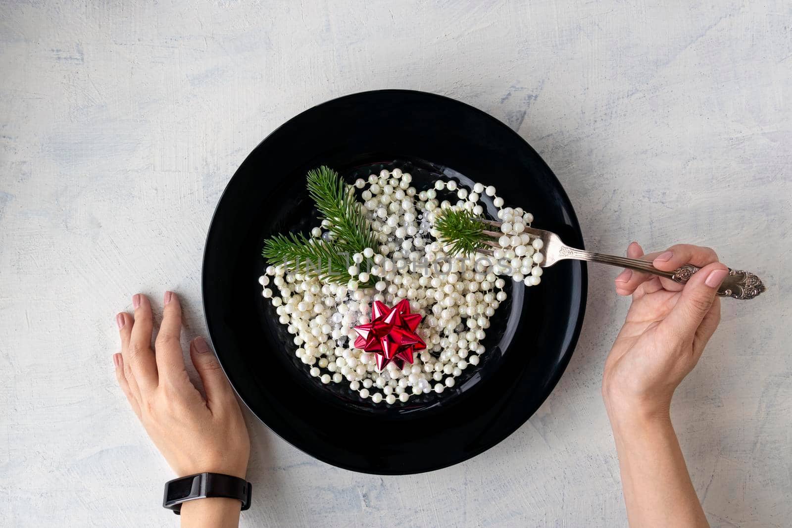 concept for christmas or new year. Christmas decorations, beads, Christmas tree branches and a red bow in a black plate, like Italian pasta. Female hands are holding a fork. top view. flat lay
