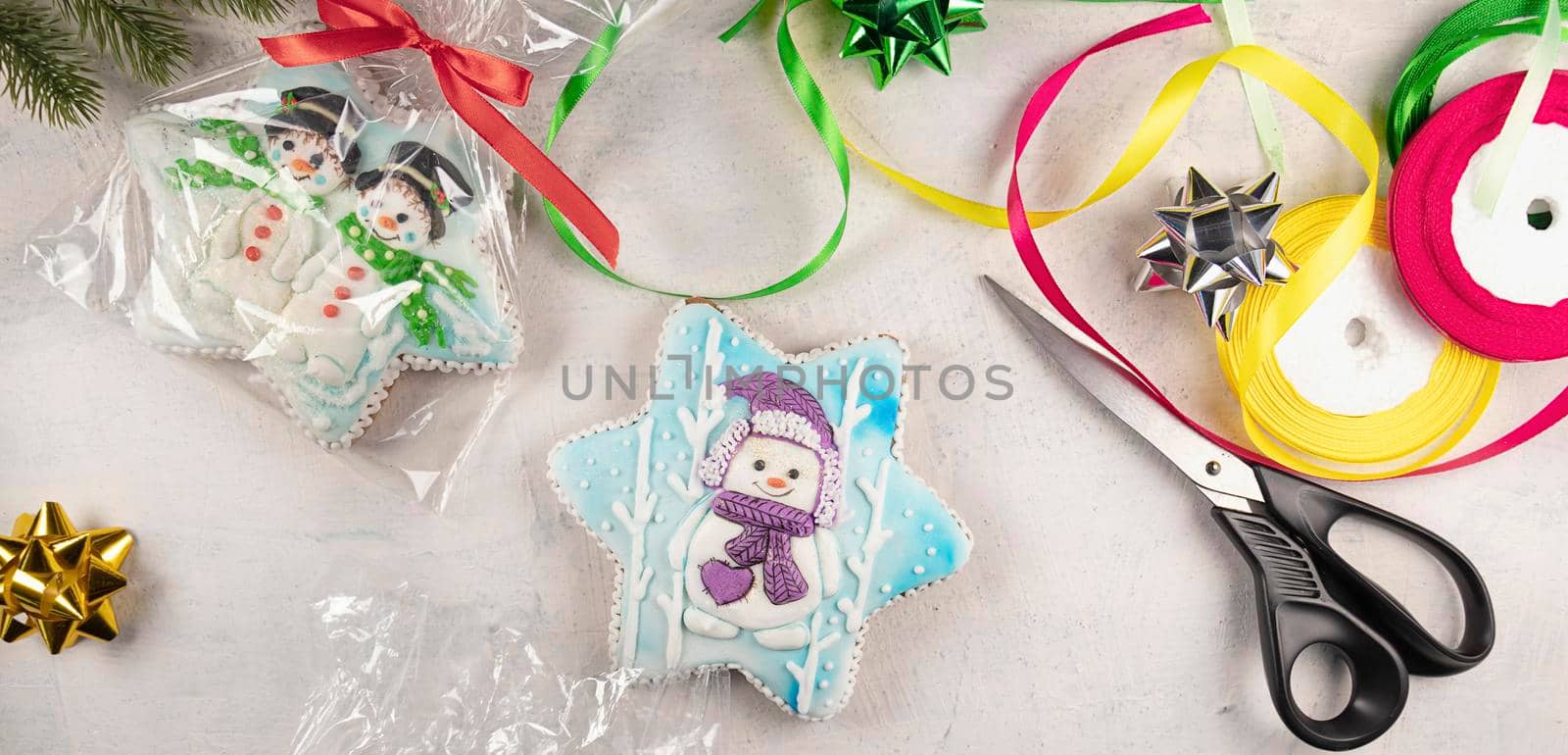 banner with packing of Christmas gingerbread cookies with snowmen on a gray background with fir branches, scissors, colorful ribbons, bows. soft focus. by Leoschka