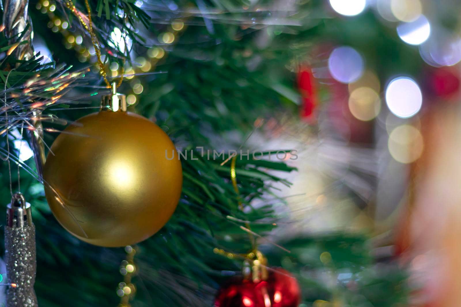 big gold christmas ball on new year or christmas background with green tree, white snowflakes, colorful toys and gold beads with bokeh and copy space. Soft focus