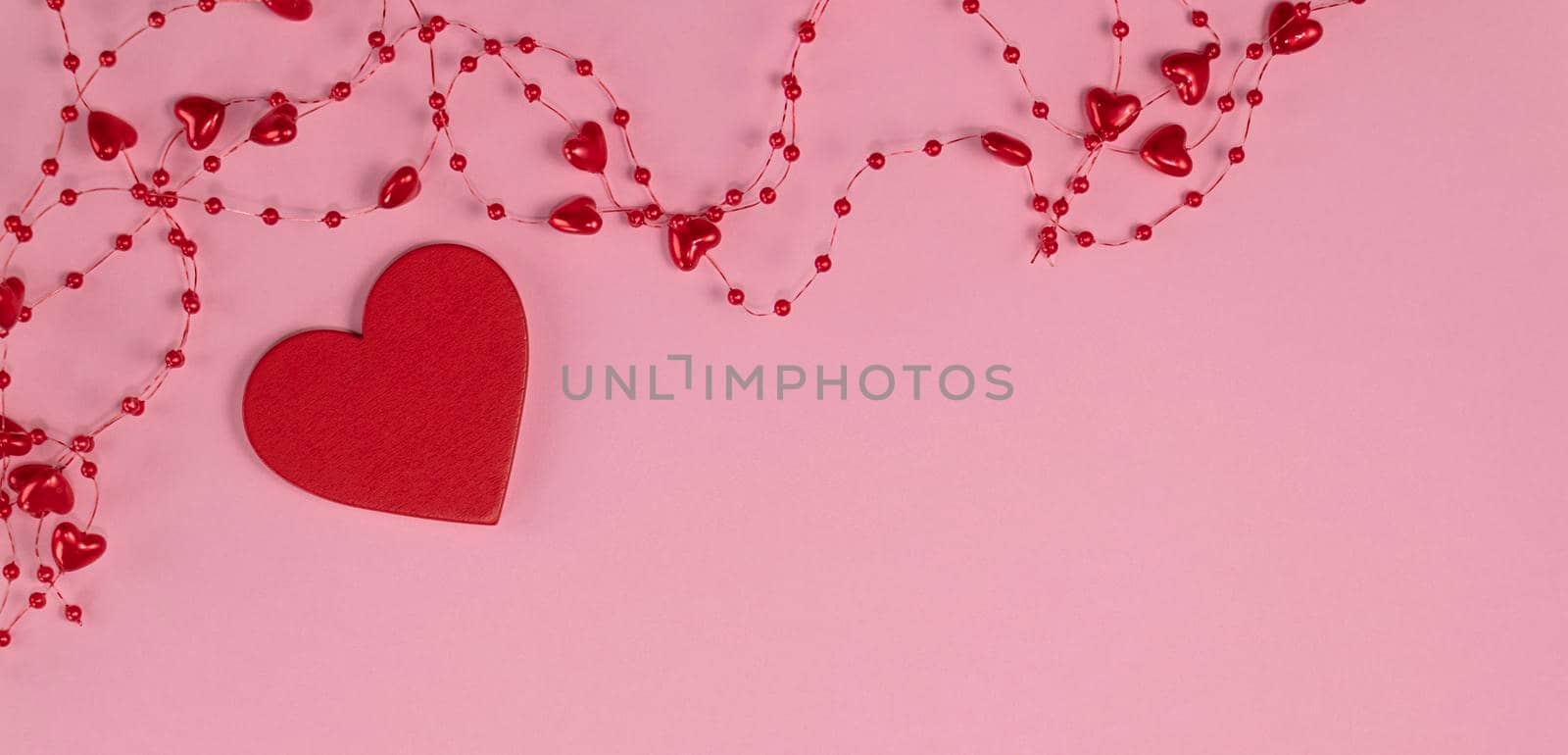 banner with concept of minimalism valentine's day. red heart on pastel pink background with red beads with hearts. Soft focus. flat lay. Copy space