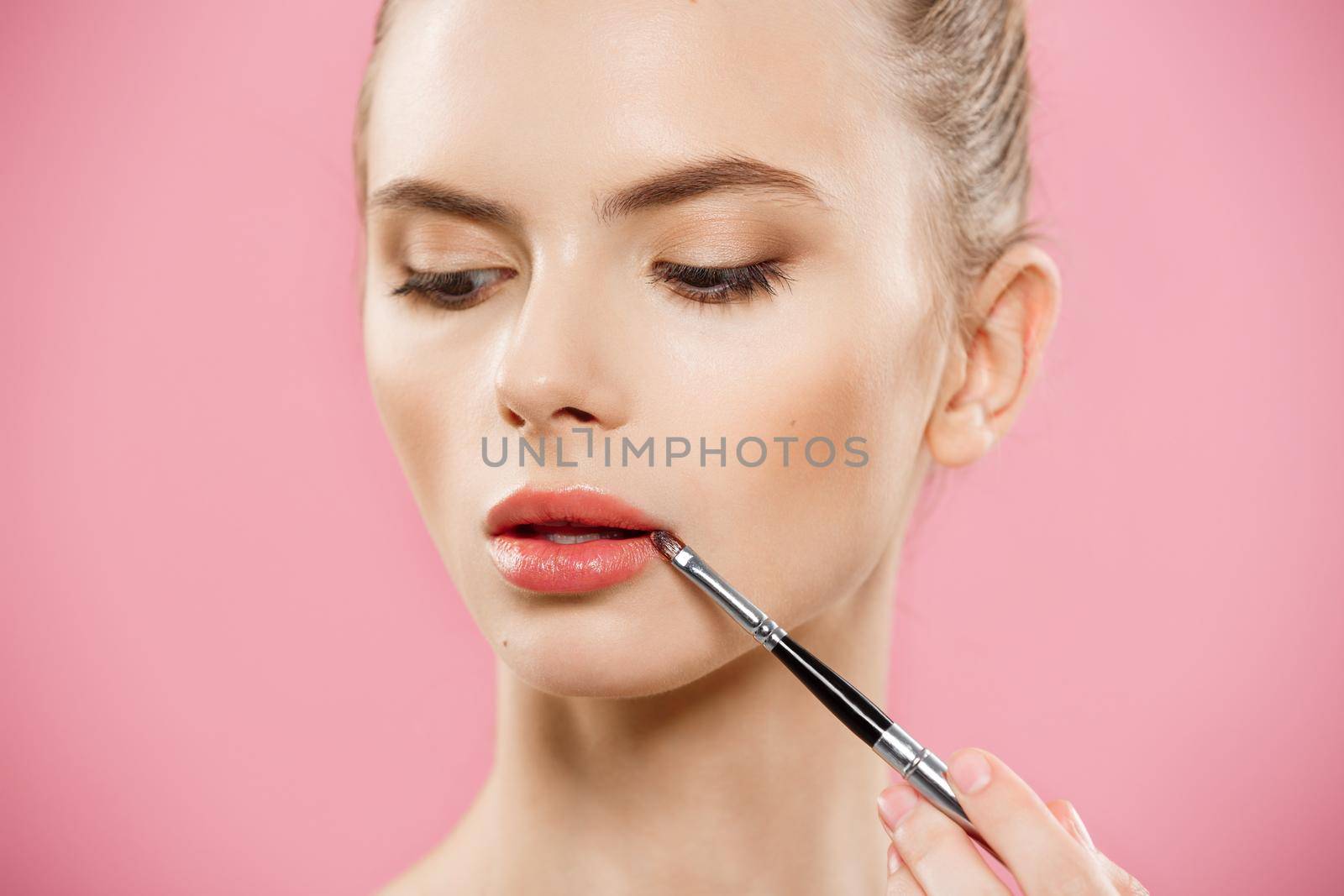 Beauty Concept - Woman applying red lipstick with pink studio background. Beautiful girl makes makeup