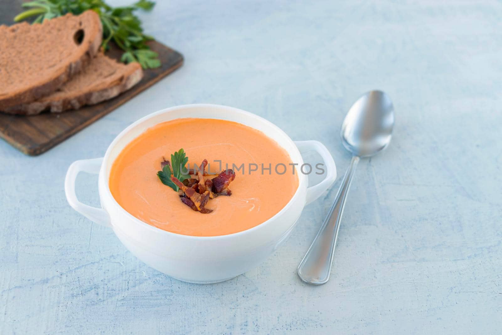 pumpkin soup with fried bacon, served in a white tureen with a spoon and slices of bread and parsley. warming hearty orange soup on a cold autumn day. copy space