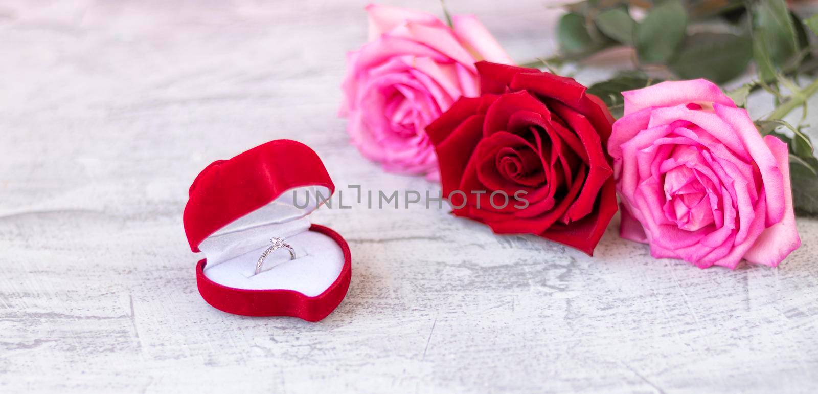banner with Wedding ring inside red velvet box for engagement ring next to a bouquet of roses with space for text. Romantic gift for Valentine's day. Marriage proposal concept. Soft focus. Copy space