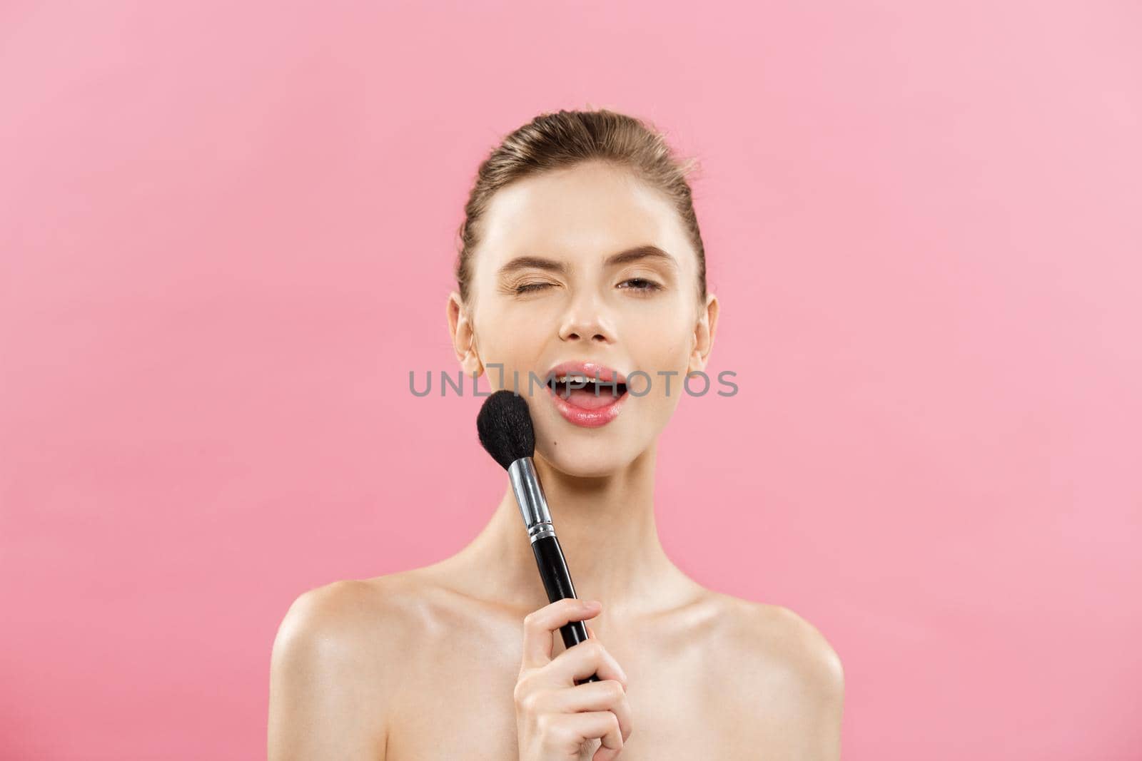 Beauty Concept - Closeup Beautiful caucasian woman applying makeup with Cosmetic Powder Brush. Perfect Skin. Isolated on pink background and copy space. by Benzoix