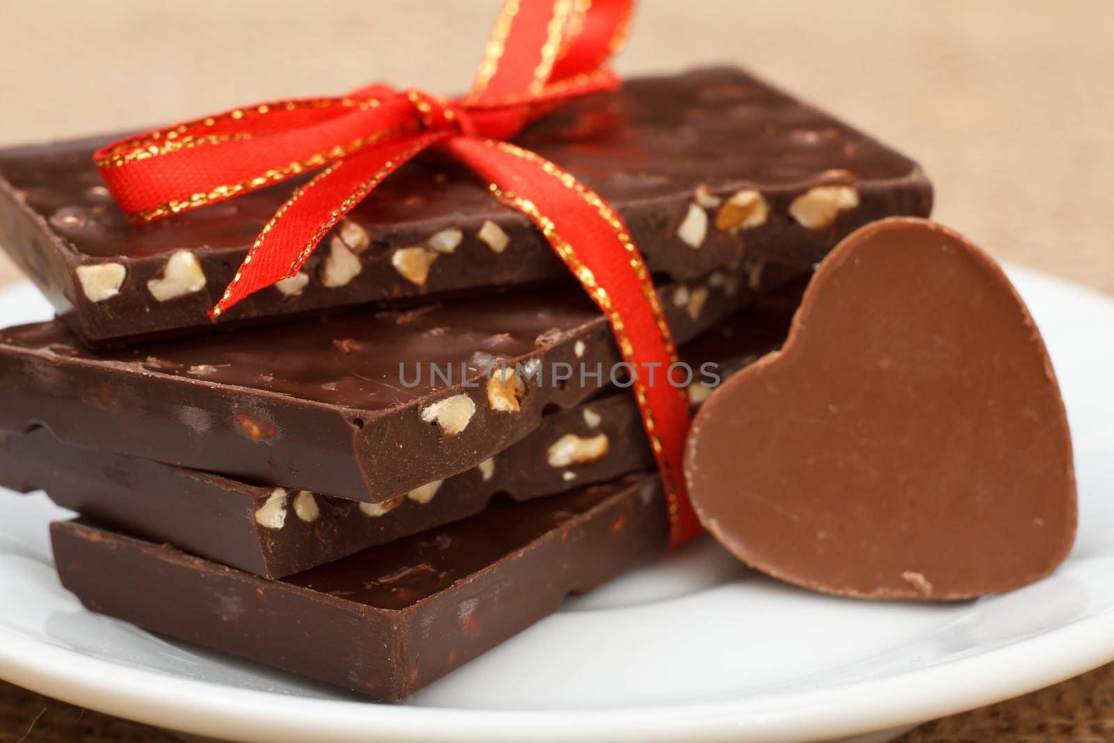 Chocolate bars with nuts and chocolate candy in shape of heart on white saucer