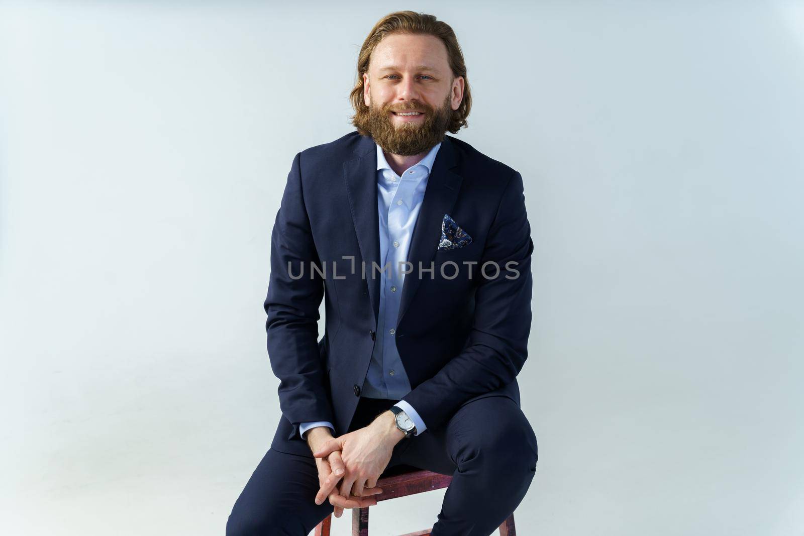 a handsome brutal bearded and long-haired man, a stylish businessman sitting on a chair with a white background. High quality photo