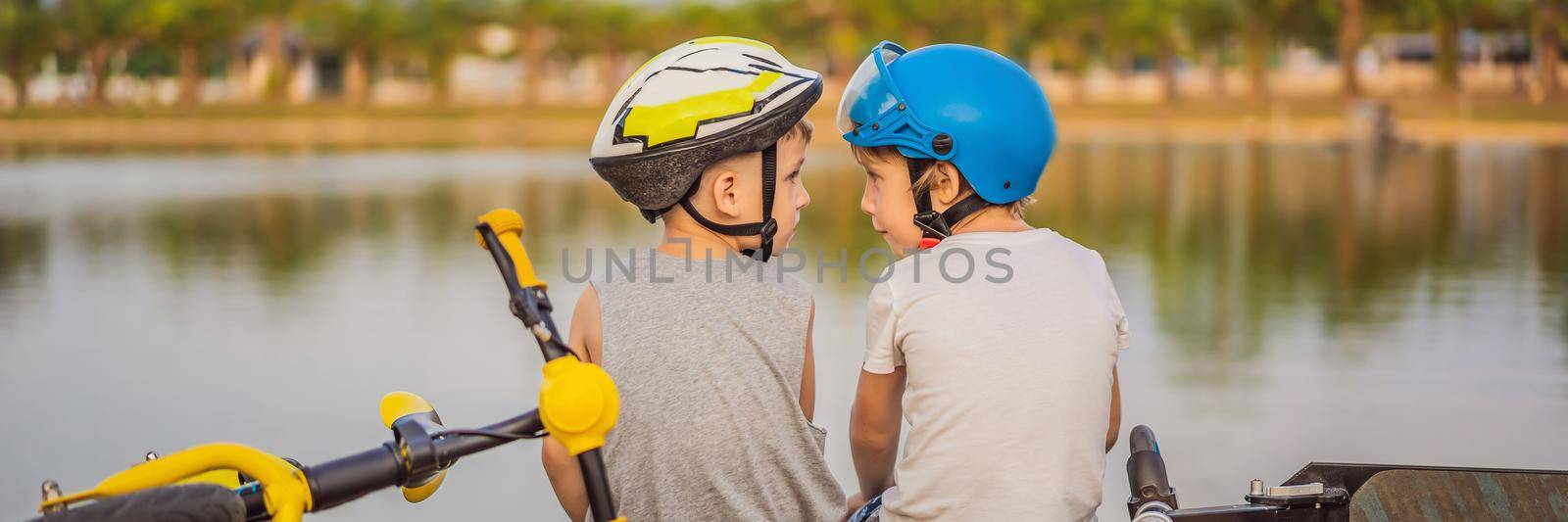 Two boys sit on the shore of the lake after riding a bike and scooter BANNER, LONG FORMAT by galitskaya