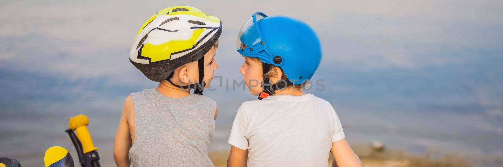 Two boys sit on the shore of the lake after riding a bike and scooter. BANNER, LONG FORMAT