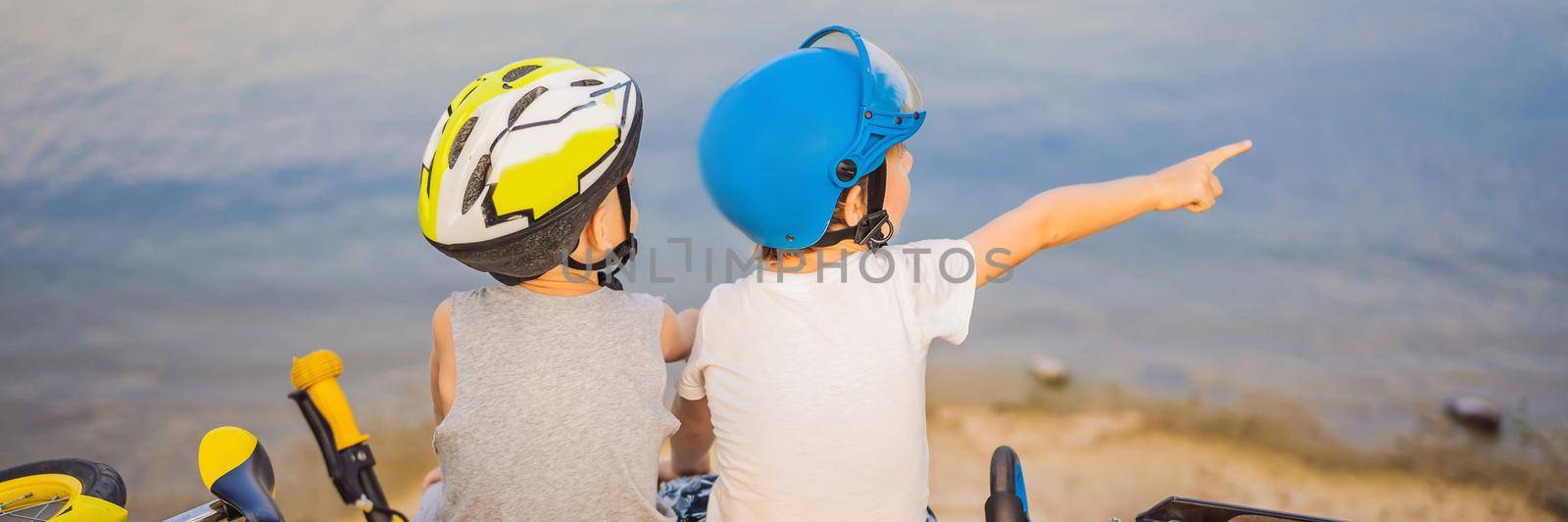 Two boys sit on the shore of the lake after riding a bike and scooter BANNER, LONG FORMAT by galitskaya