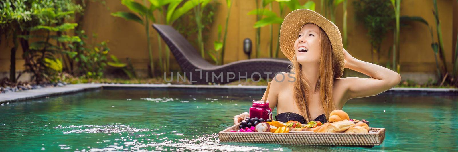 BANNER, LONG FORMAT Breakfast tray in swimming pool, floating breakfast in luxury hotel. Girl relaxing in the pool drinking smoothies and eating fruit plate, smoothie bowl by the hotel pool. Exotic summer diet. Tropical beach lifestyle. Bali Trend by galitskaya