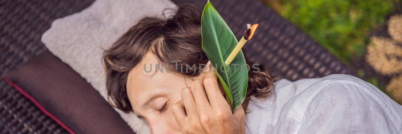 man having an ear candle therapy against the backdrop of a tropical garden. BANNER, LONG FORMAT