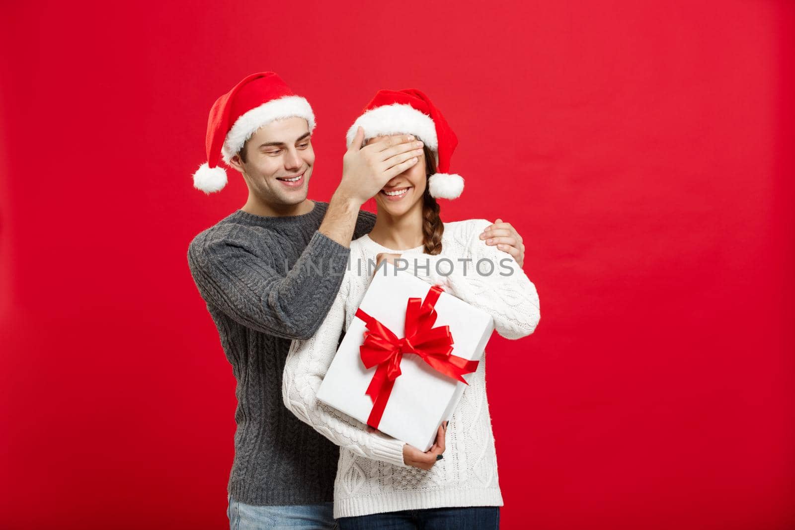 Christmas Concept - handsome young boyfriend in sweater surprise his girlfriend with white gift by Benzoix