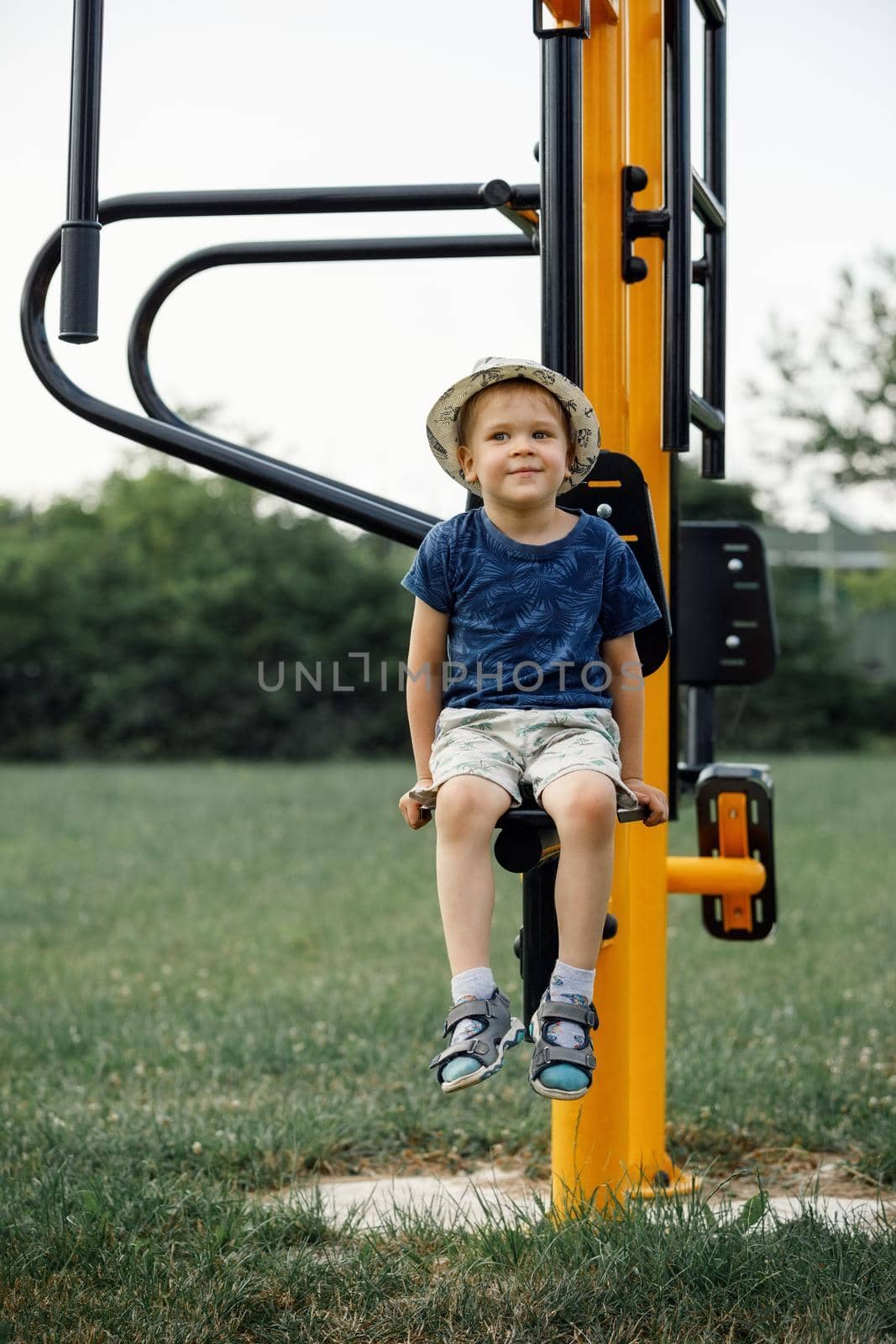 Boy athlete on outdoor sports ground. Child sitting on yellow outdoor exercise machine for teenagers.