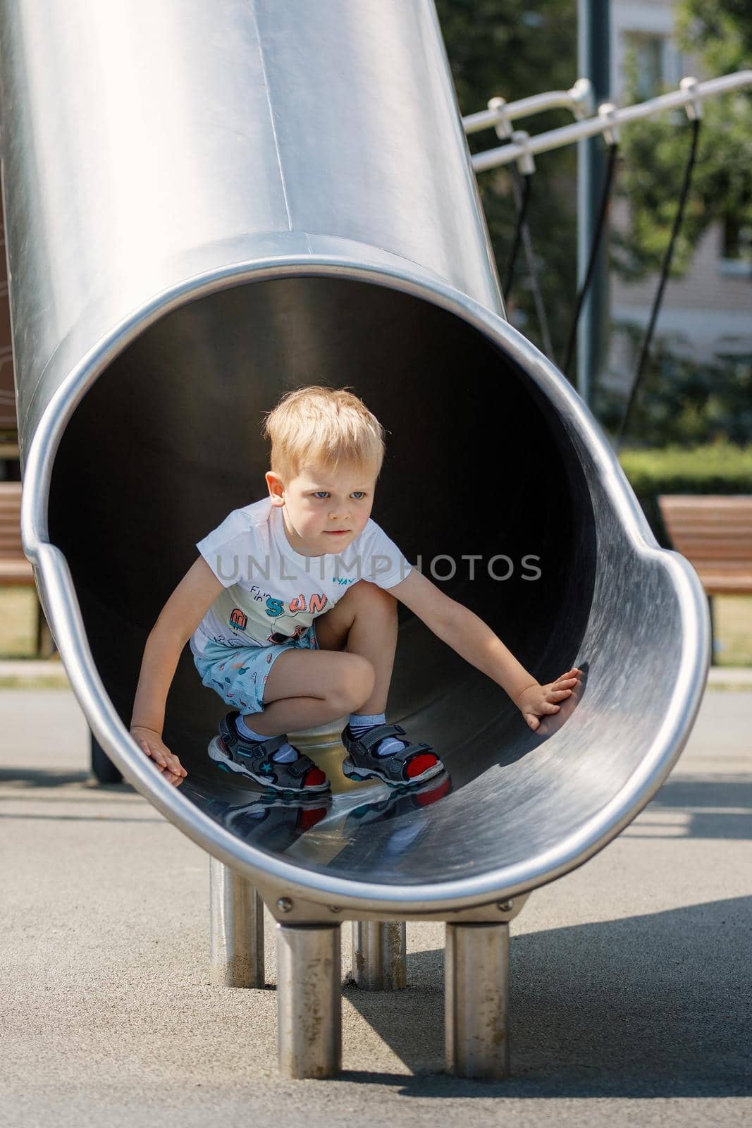 Joyful kid sliding in tube slide on playground. Kindergarten for elementary age children.