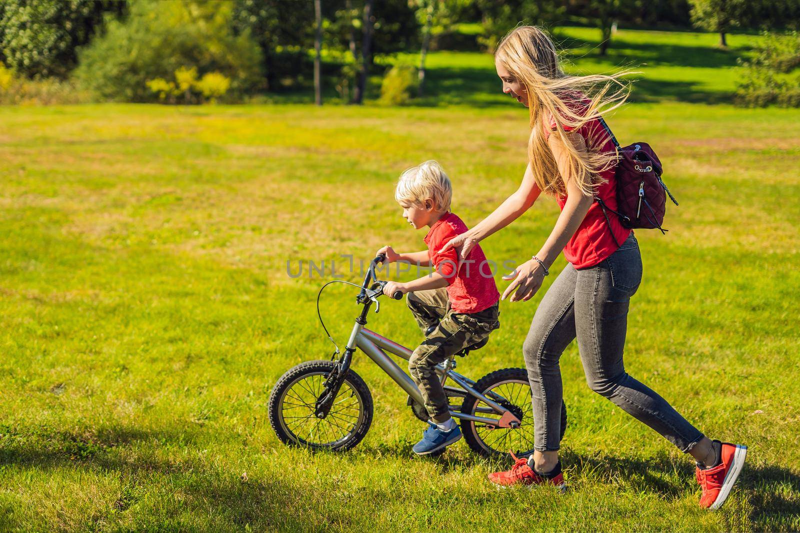 Young mother teaching her son how to ride a bicycle in the park.