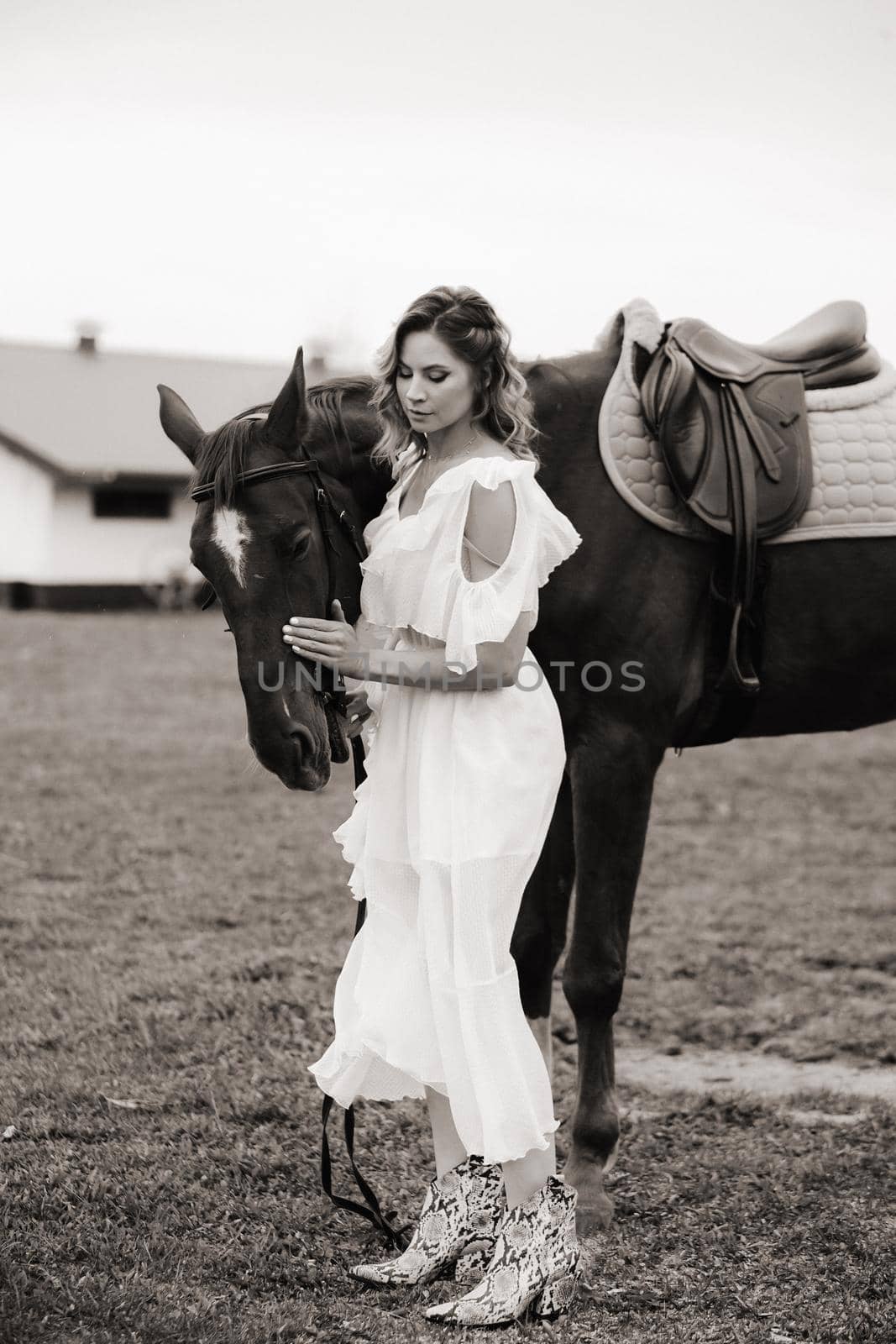 Beautiful girl in a white sundress next to a horse on an old ranch. black and white photo.