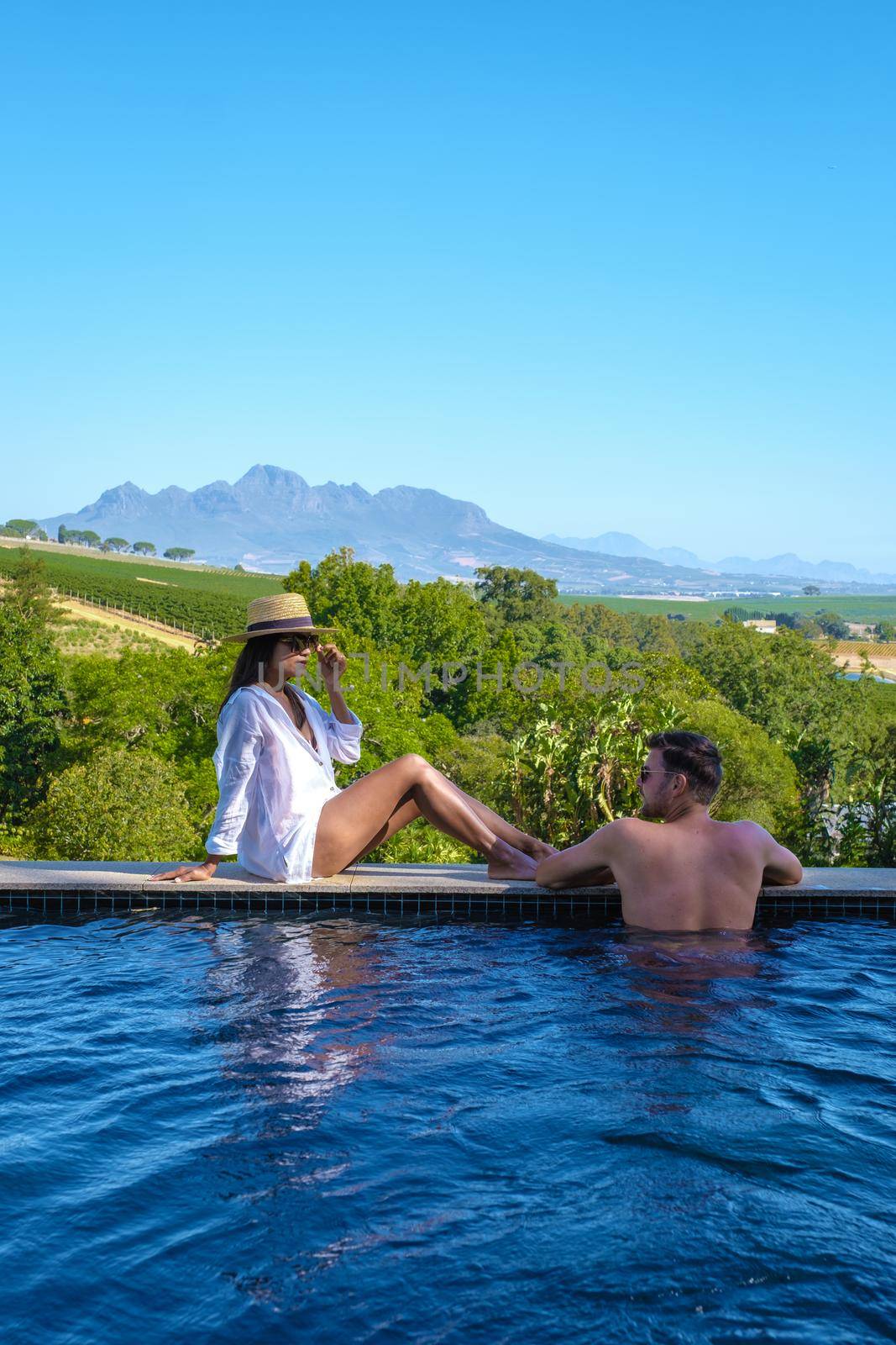couple man and women in swimming pool looking out over the Vineyards and mountains of Stellenbosch South Africa.