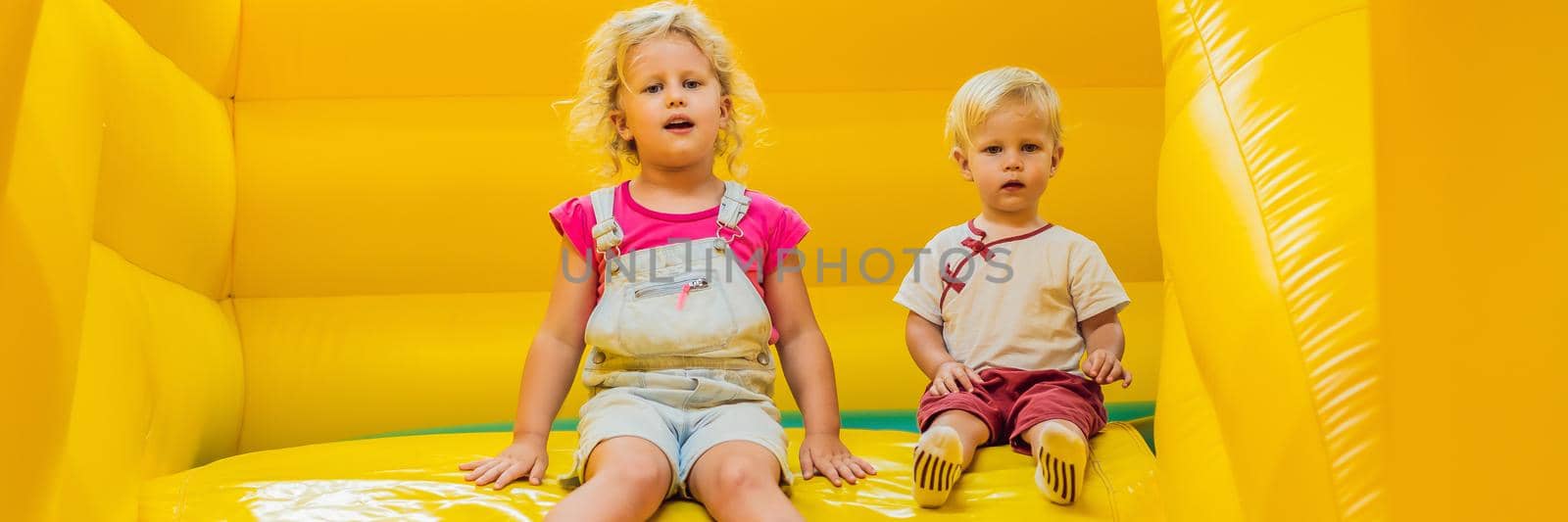 A boy and a girl ride from an inflatable slide. BANNER, LONG FORMAT