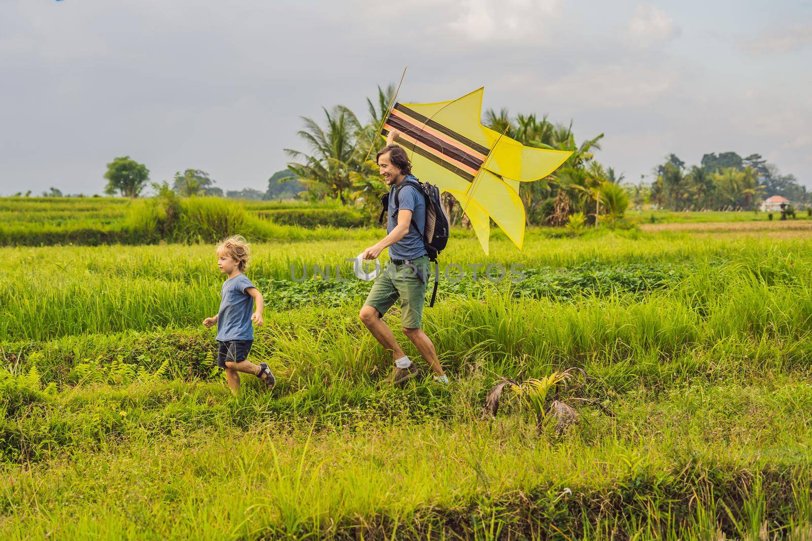 Dad and son launch a kite in a rice field in Ubud, Bali Island, Indonesia by galitskaya