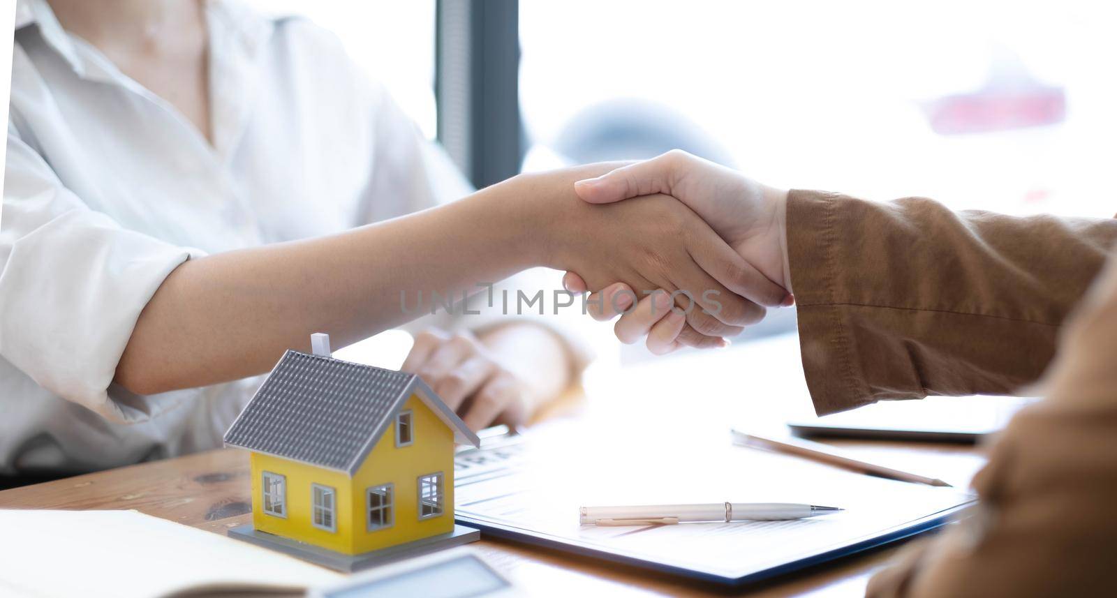 Real estate broker agent and customer shaking hands after signing contract documents for realty purchase, Bank employees congratulate, Concept mortgage loan approval..