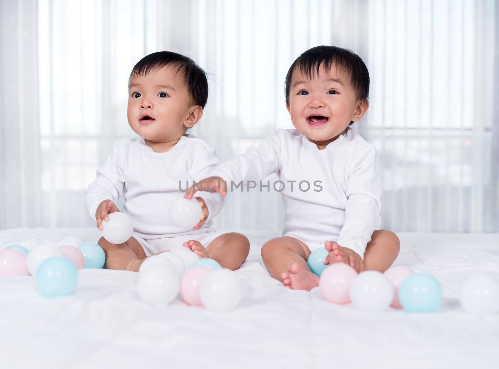cheerful twin babies playing color ball on a bed
