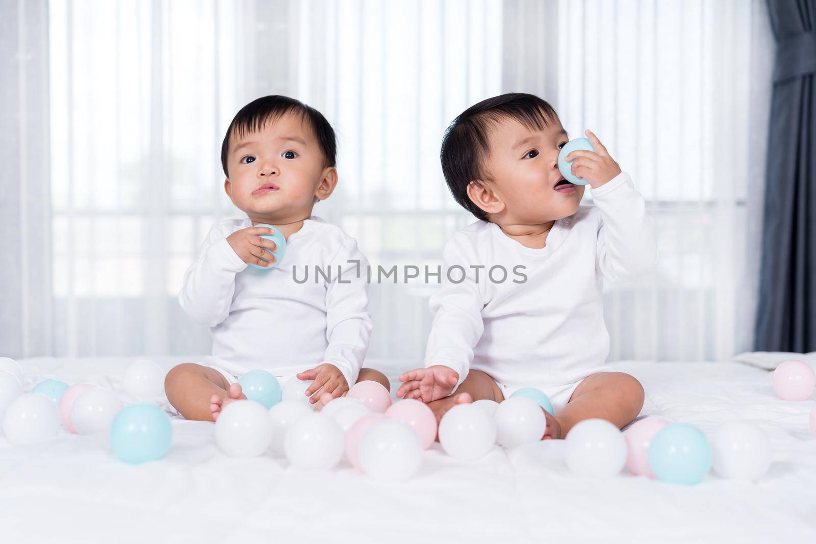 cheerful twin babies playing color ball on  bed by geargodz
