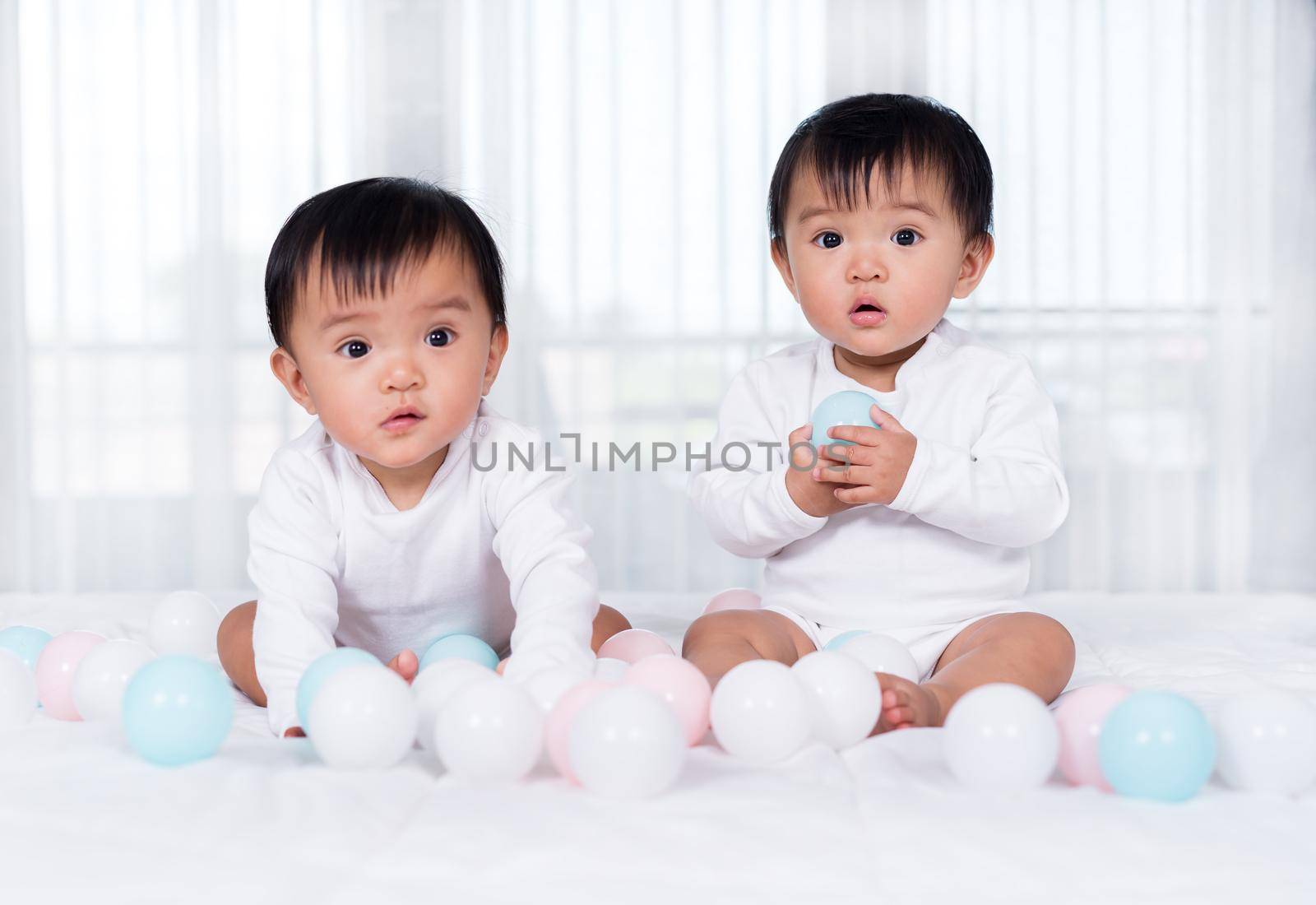 cheerful twin babies playing color ball on a bed