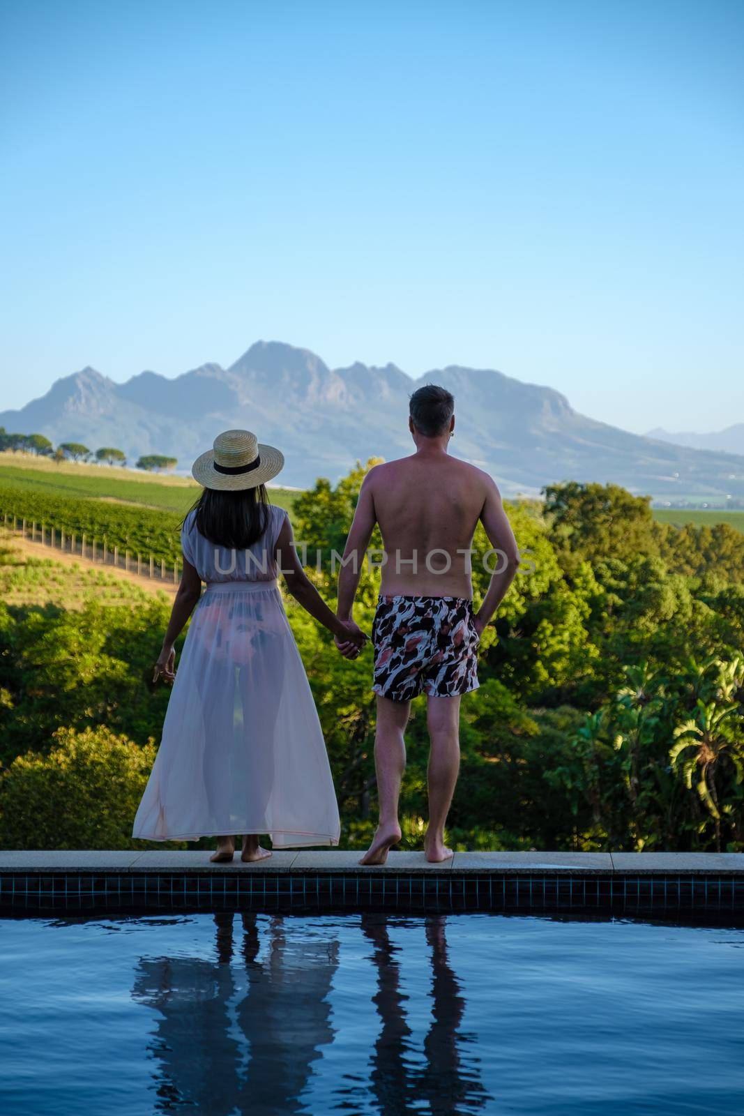 couple man and women in swimming pool looking out over the Vineyards and mountains of Stellenbosch South Africa.