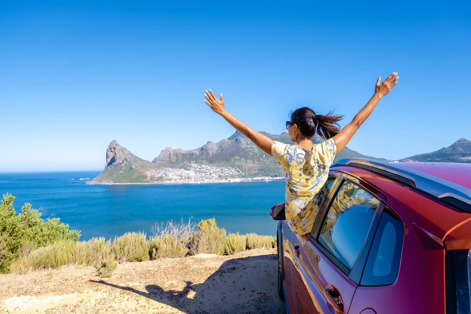 woman outside car window road trip with hands up, car at Chapmans Peak Drive in Cape Town South Africa looking out over ocean by fokkebok