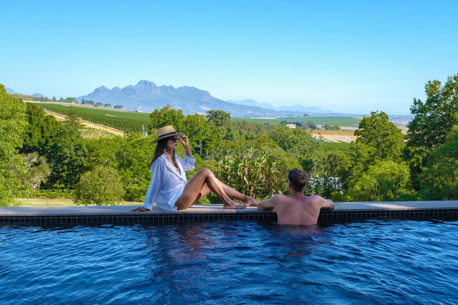 couple man and women in swimming pool looking out over the Vineyards and mountains of Stellenbosch South Africa.