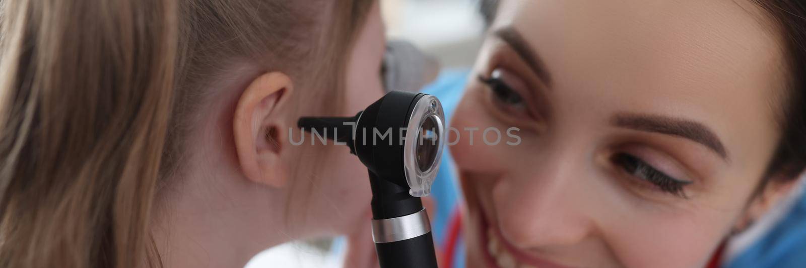 Ent woman examining ear of little girl with otoscope in clinic by kuprevich