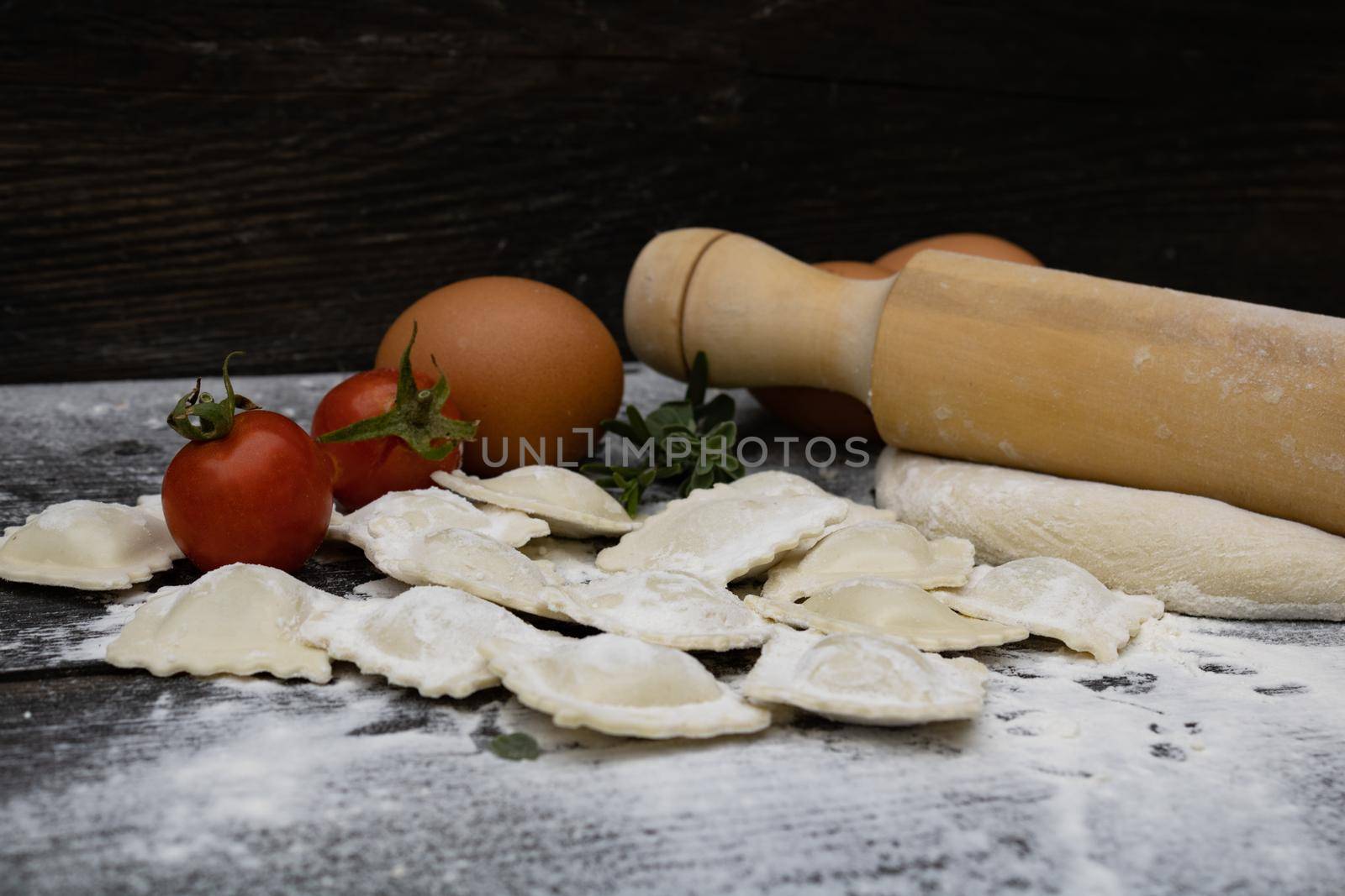 rolling pin with tomatoes, dough, eggs, flour and ravioli on wood