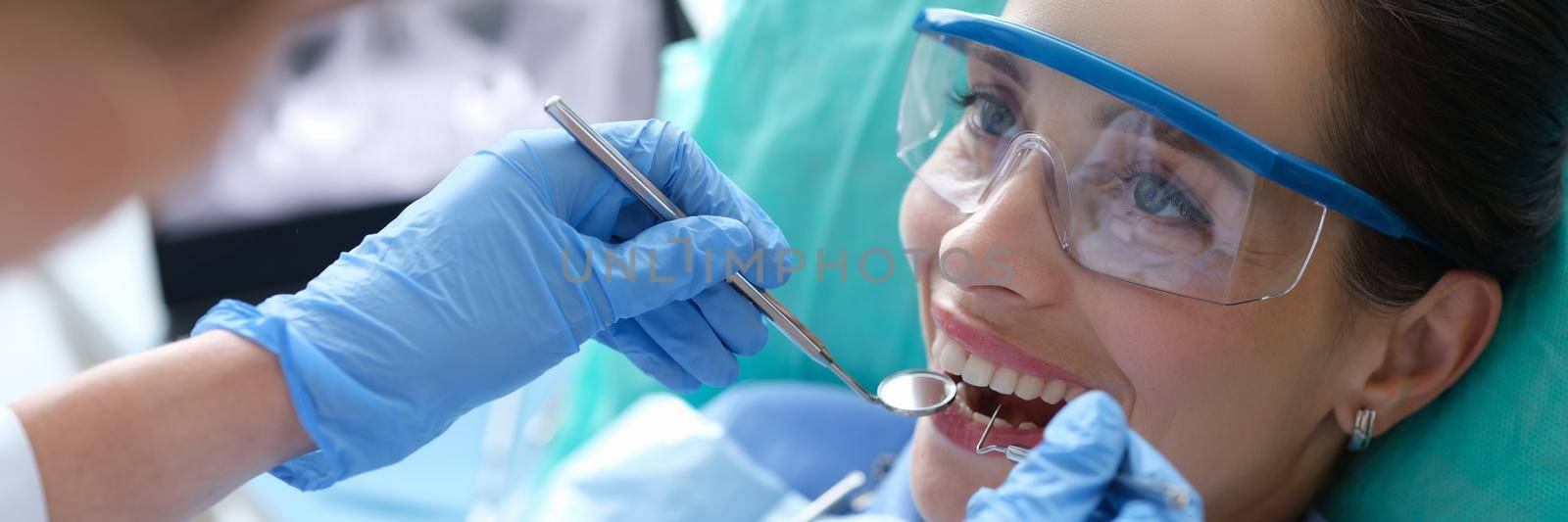 Doctor examining oral cavity of female patient using dental instruments in clinic. Annual preventive dental checkups concept